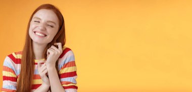 Mutlu, romantik, genç, narin kızıl kız hayal gücü yaratıyor. Gülümsüyor, seviniyor, saçlara dokunuyor, güzel anıları anımsıyor, turuncu arka planda duruyor..