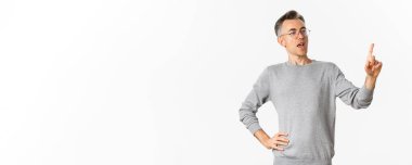 Gri süveter ve gözlüklü kendinden emin orta yaşlı işadamının resmi. Parmakla gösterip konuşma yapıyor, çalışanlara görevler veriyor, beyaz arka planda duruyor..