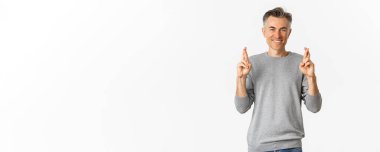 Umut dolu orta yaşlı bir adamın dilek tutması, şans dileyip gülümsemesi, iyi haberler beklemesi, beyaz arka planda durması..