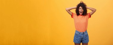 Kız panik içinde erkek arkadaşlarıyla tanışmaya hazır değil. Şok olmuş sıkıntılı ve endişeli bir kız arkadaşın portresi afro saç stili ile el ele tutuşmuş turuncu arka planda şok geçirip bağırıyor.