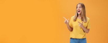 Neşeli, şevkli, karizmatik, sarı saçlı, bronz tenli, makyajsız, turuncu arka planda neşeli bir gülümsemeyle sol üst köşeye bakan bir kız. Vücut dili