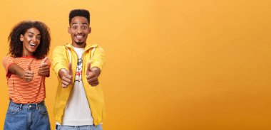 İki arkadaş mükemmel ve harika planı sever. Neşeli, dost canlısı, iyimser görünümlü, Amerikalı kadın ve erkeğin onaylama ve uzlaşma jestlerinde başparmak gösteren portresi geniş bir gülümsemeyle. Anlaşıldı.