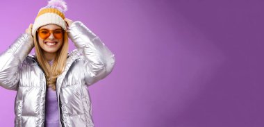 Enerjik, küstah, genç ve çekici bir kadın kış gezisinde eğleniyor. Snowboard yapmayı öğreniyor. Yüzsüz bir şekilde gülümsüyor, tatilde şapkasını takıyor..