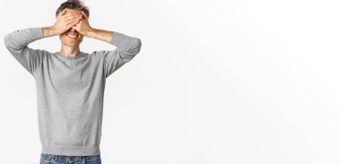 Yakışıklı, mutlu, orta yaşlı bir adamın portresi şaşırmayı bekliyor, gözleri kapalı, gülümsüyor, saklambaç oynuyor, beyaz arka planda duruyor..