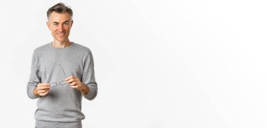 Gri kazaklı, yakışıklı ve kendine güvenen bir adamın portresi. Gözlüklerini çıkarıyor ve gülümsüyor..