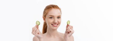 Yüzüne salatalık dilimleri tutan, gülümseyen, yarı çıplak bir kadının güzel portresini kapat. Beyaz arka planda izole edilmiş..