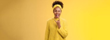 Heyecanlı, güler yüzlü, cesur, Afro-Amerikan kadını eğlence şovu yapıyor rock-n-roll heavy metal jestleri yapıyor harika bir partiden keyif alıyor, sarı arka planda duruyor..