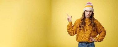 Berbat bir tanıtım. Portre seçici, kibirli, etkilenmemiş, bayan modaya uygun, üst sol köşeyi gösteren, hoşnutsuz, hoşnutsuz, kötü tekliften hoşlanmayan, sarı arkaplan..