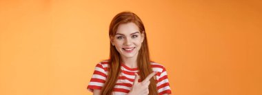 Yan tarafı gösteren neşeli, yakın plan bir kız. Kızıl saçlı kadın iyi bir teklif sunar, ilginç bir şekilde sırıtır sol üst köşede, turuncu arka planda..