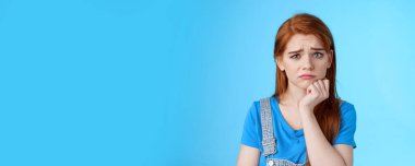 Üzgün, tatlı, tedirgin, tatlı kızıl saçlı, kaşlarını çatan, hayal kırıklığına uğramış suratını buruşturan, acınacak haldeki, sızlanan, şikayet eden, piyangoyu kaybeden, mavi arka plan kederli bir kız. Boşluğu kopyala