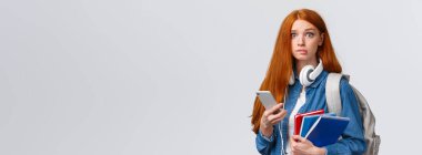 Kararsız, gergin, tatlı, birinci sınıf öğrencisi kız, yeni yıla başla, endişeli bir kamera gibi görün, dudaklarını ısırma, sırt çantası, not defterleri ve akıllı telefon, mesaj okuma..