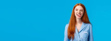 Kaygısız ve komik kızıl saçlı genç kız pijama partisi sırasında uyumak istemiyor. Dilini gösterip aylak aylak dolaşmak, dalga geçmek, neşe içinde göz kırpmak, gece kıyafeti giymek, mavi arka plan..