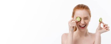 Yüzüne salatalık dilimleri tutan, gülümseyen, yarı çıplak bir kadının güzel portresini kapat. Beyaz arka planda izole edilmiş..