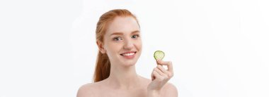 Yüzüne salatalık dilimleri tutan, gülümseyen, yarı çıplak bir kadının güzel portresini kapat. Beyaz arka planda izole edilmiş..