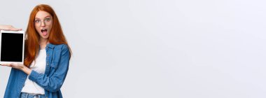 Heyecanlı ve eğlenceli kızıl saçlı genç kız tasarım yapıyor, cihaz ekranında yaratıcı proje, dijital tablet ekranını gösteriyor, şaşırmış görünüyor, ağzı açık, beyaz arka plan.