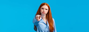Alıngan, çekingen ve aptal kızıl saçlı genç, kameraya suçlayan, utandıran, somurtan, somurtan, somurtan, suçlayan, memnun olmayan, mavi arka planda duran biri..