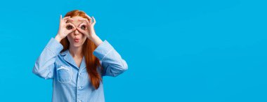Kız diyor ki, vay canına kameraya bakıp özel tatil indirimi için harika bir fırsat yakalamış. Pijamalı çekici kızıl saçlı kadın parmaklarından ve kıvrılmış dudaklarından bakıp eğleniyor, mavi arka plan.