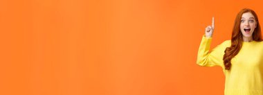 Kış tatillerinde yurtdışına seyahat eden heyecanlı bir kız, zaman valizi. Şaşırmış ve sevimli kızıl saçlı kadın mutluluğunu ifade ediyor, satışa işaret ediyor, promosyon ve gülümseme büyülenmiş, turuncu arka plan.