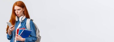 Memnun değil, kızgın ya da kafası karışık güzel bir üniversiteli kız sırt çantası, not defterleri ve kulaklıkları olan bir öğrenci akıllı telefondan garip mesajlar okuyor, üzgün, beyaz bir geçmişi var..