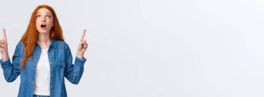 Belden yukarısı portresi şaşırmış ve etkilenmiş, meraklı kızıl kız mağazada harika bir oyuna bakıyor, çenesini indiriyor, nutku tutulmuş, nefes nefese kalmış, beyaz arka planda duruyor..