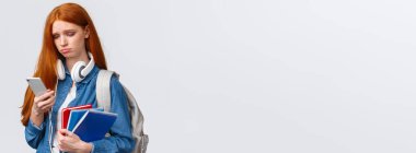 Aptal, üzgün, kasvetli, kızıl saçlı, kaşlarını çatmış, pişmanlık dolu, akıllı telefon ekranına bakıp rahatsız edici mesajlar okuyan, kötü hisseden, sırt çantalı ve defterli bir kız..