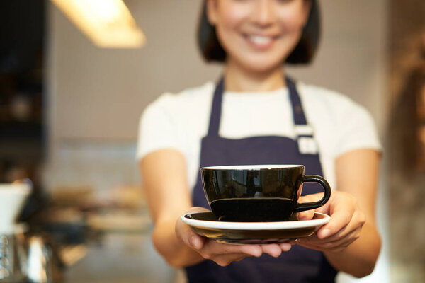 Cropped shot, female barista hands holding cup of coffee, giving you drink, serving in cafe, wearing uniform.