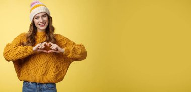 Kız barış getirir sevgi gösterisi kalp hareketi baş eğme gülümseme sempati ifade etme tutku sevgili sıcak duygular, kalp işareti, sırıtan flört, sarı arka plan.