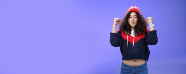 Çekici 20 'li yaşlarda, kıvırcık saçlı, sıcak bere takmış, elini kaldıran, tişörtünün altında zafer kazanan, muhteşem zaferi kutlayan, mavi arka planda sevinç ve heyecandan dudaklarını kıvıran bir kız..