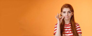 Kız sır saklayabilir. Ciddi görünümlü kızıl saçlı bayan arkadaş kimseye söylemeyeceğine söz veriyor, fok ağzı, jest, iddialı ve kararlı görün, sessiz kal, turuncu arka planda dur..