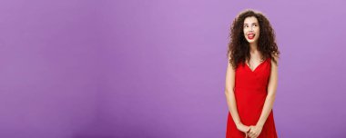 Studio shot of cute thoughtful and creative charming european woman in stylish red licking lips with desire and amusement looking at upper right corner smiling, daydreaming using imagination. Copy