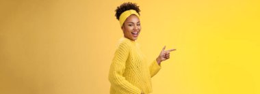 Şımarık, Afro-Amerikan kadın 20 'li yaşlarda, saç bandı kazaklı, sırıtkan, cilveli bakışlı, kameralı, ayakta duran, profil oluşturan, sola bakan, harika, yeni bir ürün, sarı arka plan..