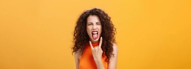 Kaygısız, asi, şık, kıvırcık saçlı kadın. Dilini çıkarıp sevinçten bağırarak rock 'n roll tabelasını serinletiyor ve turuncu arka planda serin konserin tadını çıkarıyor..