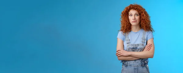 Lifestyle. Unsure confused redhead curly woman look perplexed uncertain cross arms chest smirking stare camera full disbelief suspicious doubtful someone telling truth standing denim overalls blue