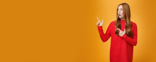 Impressed and curious good-looking stylish 20s redhead woman with cute curls in red dress drop jaw from amazement and interest as looking and pointing at upper left corner speechless. Advertisement
