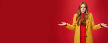 Üzgün ve kafası karışık olan kızıl kız arkadaş ellerini yana doğru uzatarak ne olduğunu anlayamaz ve nedeninin farkında olmadan yüzünü buruşturur, kırmızı duvarın üzerinde endişeli bir şekilde poz verir. Vücut dili ve