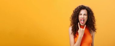 Kaygısız, asi, şık, kıvırcık saçlı kadın. Dilini çıkarıp sevinçten bağırarak rock 'n roll tabelasını serinletiyor ve turuncu arka planda serin konserin tadını çıkarıyor..