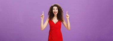 Hayalperest, hevesli, çekici genç bir kadının portresi. Kıvırcık saçlı, kırmızı şık elbiseli, kollarını kaldıran, gülümseyen, neşe ve mutlulukla mor duvarın üzerinde poz veren..