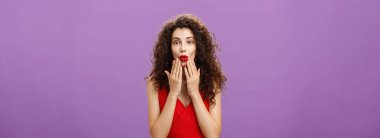 Zevkli ve heyecanlı, lüks, kıvırcık saçlı yetişkin kadın. Akşam makyajı kırmızı elbiseyle dudaklarını katlayarak avuçlarını yüzüne dayayarak mor duvarın ardındaki ilginç söylentileri dikkatle dinlerken..