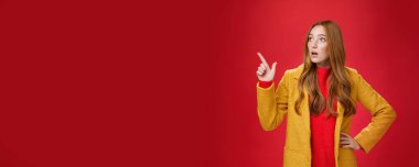 Yaşam tarzı. Empatik bir portre, şaşırmış ve şaşırmış sarı montlu kızıl saçlı kadın ağzı açık, şaşkın ve nutku tutulmuştu. Sol üst köşeyi işaret ediyor ve endişeli ve kırmızı duvarın üzerinden titriyordu..