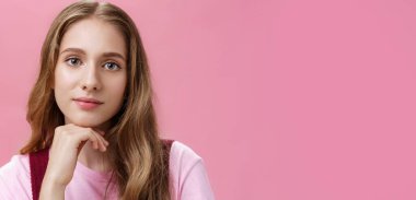 Çekici, alımlı, doğal saçları dalgalı, çenesinde hafif makyajı olan ve pembe duvarın üzerinde rüya gibi, dostane bakışlarla gülümseyen genç bir kızın yakın çekimi. Boşluğu kopyala