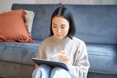 Tablet ve kalemle oturmuş dijital uygulamayı çizen yaratıcı genç bir kadın..