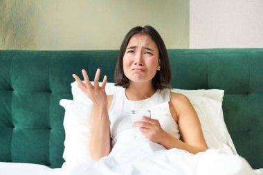 Hayal kırıklığına uğramış Asyalı kız, ağlıyor ve sızlanıyor, üzgün hissediyor, yastığa uzanmış, cep telefonunu tutuyor, kötü haberleri okuyor, korkunç bir ruh haliyle uyanıyor..