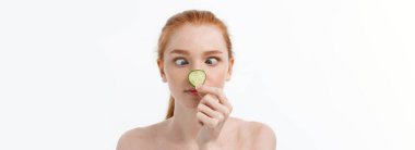 Yüzüne salatalık dilimleri tutan, gülümseyen, yarı çıplak bir kadının güzel portresini kapat. Beyaz arka planda izole edilmiş..