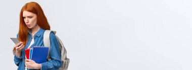 Bu da ne? Kafası karışık ve hoşnutsuz. Sorunlu kızıl saçlı genç, sırt çantası ve defterleri olan üniversiteli kız üniversitede yürüyor ve akıllı telefondan garip mesajlar okuyor, beyaz arka plan..