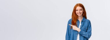 İhtiyacımız olan şey burada. Kot gömlekli neşeli kızıl kadın, sol fotokopi alanını işaret ediyor, gülümsüyor iyi ürün öneriyor, inceleme hizmeti veriyor, web sitesini gösteriyor, beyaz arka plan duruyor..