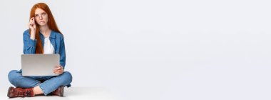 Ciddi görünümlü, zeki ve yaratıcı kızıl saçlı, sınıf için önemli bir proje üzerinde çalışan, bacak bacak üstüne atmış, dizüstü bilgisayar kullanan, dudak ısıran ve kaşlarını çatan,.