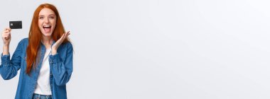 Karizmatik, mutlu, güzel, günlük kıyafetler içinde, yüzünde ışıl ışıl bir gülümsemeyle kredi kartı tutan, şaşırmış ve memnun olmuş, maaş alan, banka teklifleri gibi, beyaz arka plan.