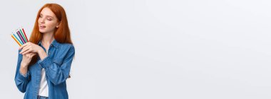 Yaratıcı ve marifetli güzel bir kadın kot gömlekli, renkli kalemler seçen, gülümseyen, ne çizdiğini düşünen, sanat eserleri yaratan, beyaz arka planda duran düşünceli..