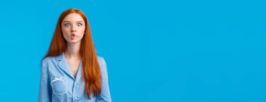 Balık gibi sessiz. Sevimli ve komik kızıl saçlı, uzun kızıl saçlı, dudaklarını taklit ederek emen, neşeli bir şekilde oynaşan, gece elbisesi giyen, mavi arka planda duran,.