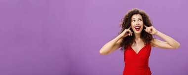 Gürültülü patlama ve havai fişekler için bekleyen kadın sağ üst köşeye sırıtarak bakıyor. İşaret parmaklarıyla kulakları kaplayan lüks kırmızı elbiseler ve akşam makyajıyla büyülenmiş..